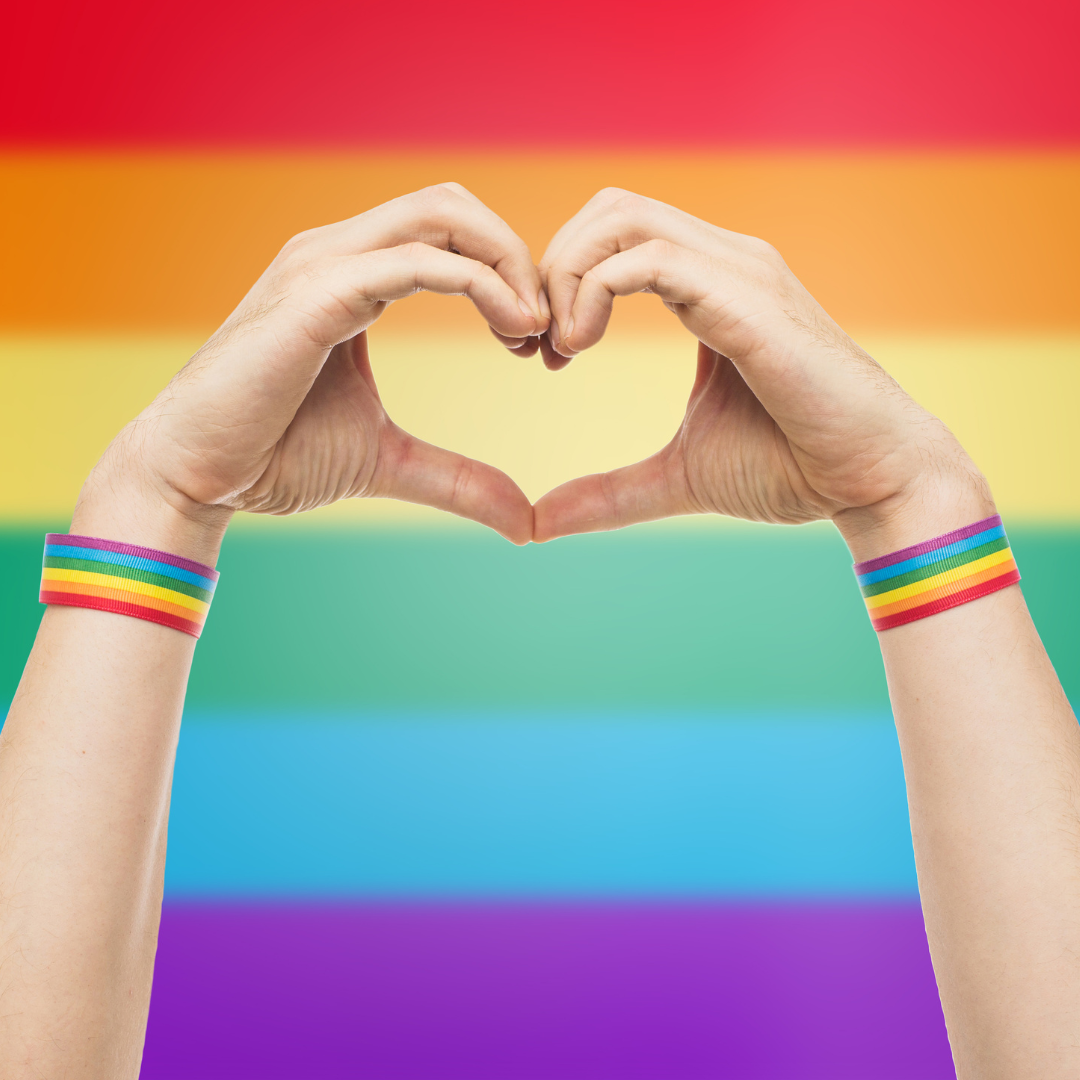 hands form a heart in front of a rainbow flag