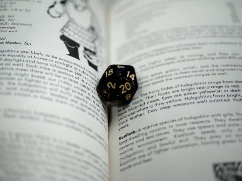 A picture of a 20-sided die nestled in the pages of a tabletop roleplaying game book. 